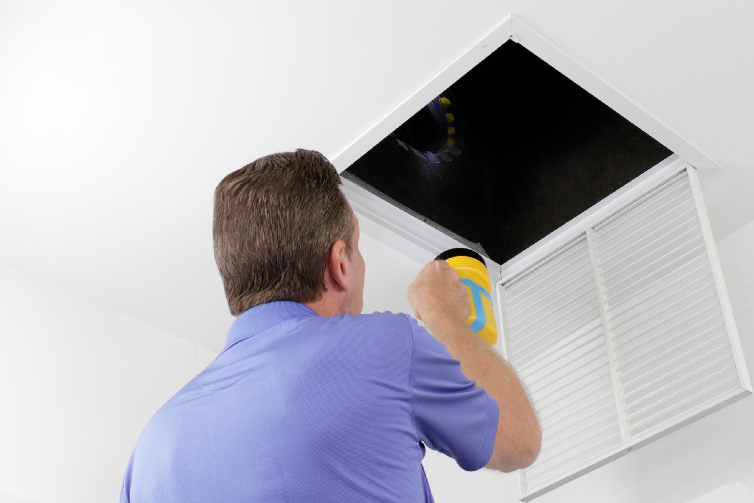 Man Inspecting An Air Duct With A Flashlight.older Male With A Yellow Flashlight Examining Hvac Ducts In A Large Square Vent. Male Technician Looking Over The Air Ducts Inside A Home Air Intake Vent.